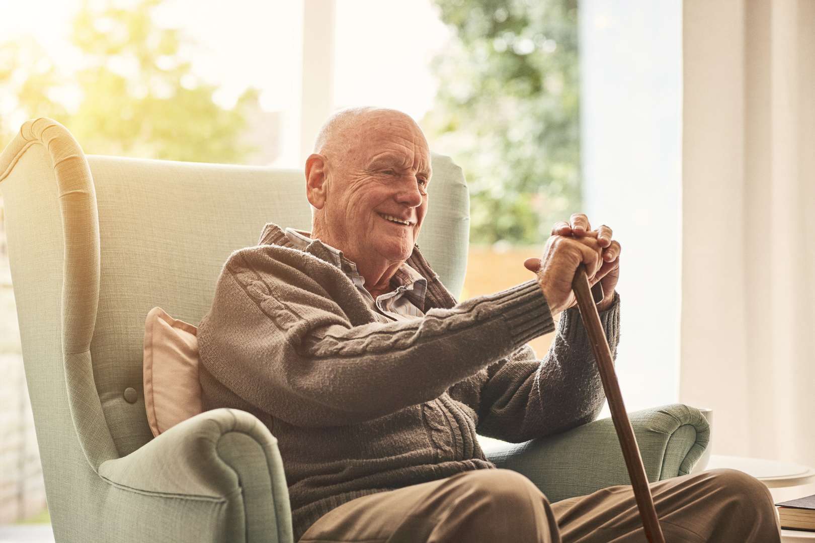 Senior man sitting in chair smiling holding a cane.